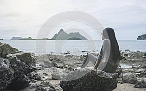 Young asian woman sitting on a rock near the sea,looked to the sea,chill out of summer,rest time,light effect added