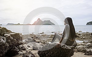 Young asian woman sitting on a rock near the sea,looked to the sea,chill out of summer,rest time,light and flare effect added