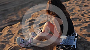 A young Asian woman is sitting on a snowboard on the sand in the outfit for a snowboard. Sandboarding. Slow Motion
