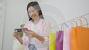 Young asian woman sitting on sofa using smart phone shopping online with credit card buying to internet.