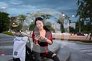 Young woman sitting on stairs in urban city at night and using smart phone.