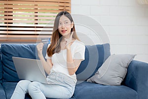 Young asian woman sitting thinking idea using credit card with laptop computer on couch.