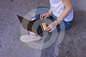 Young asian woman sitting while using a laptop and credit or debit card at public place outdoors for online shopping. Lifestyle,