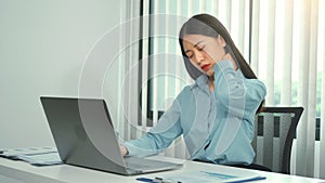 Young asian woman is sitting at work and has pain in her neck while she is sitting in the office working