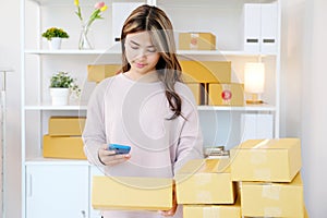 Young asian woman ,small business owner scaning product stock by mobile phone at home office