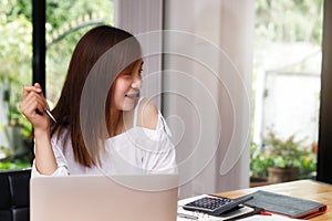 Young asian woman in smart casual wear with laptop looking outside the window in home office