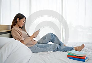 Young asian woman with a smile touching tablet computer screen in her hand while relax on bed at home, after reviewing the