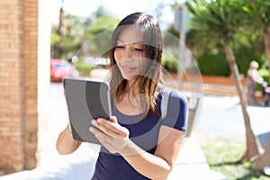 Young asian woman smiling confident using touchpad at street