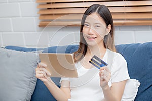 Young asian woman smiling holding credit card shopping online with tablet computer buying and payment.