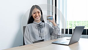 Young asian woman smiling and presenting credit card in her hands