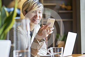 Young Asian woman smiling using smart phone and laptop at coffee shop