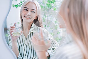 Young Asian woman spraying perfume in front of mirror