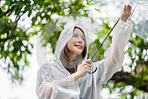 Young asian woman spreading umbrellas playing in the rain, she is wearing rainwear