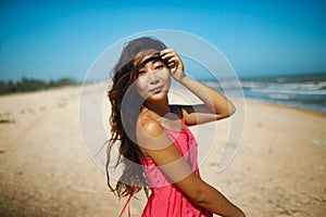 Young asian woman standing at beach. beautiful young woman in a pink dress walking back from the beach.