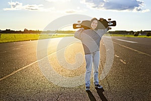 Young asian woman standing with longboard on sunny road, skating in skate park on her cruiser