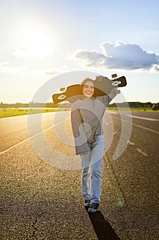 Young asian woman standing with longboard on sunny road, skating in skate park on her cruiser