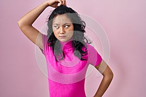 Young asian woman standing over pink background confuse and wondering about question