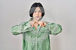 Young asian woman standing over white background rejection expression crossing fingers doing negative sign