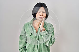 Young asian woman standing over white background touching mouth with hand with painful expression because of toothache or dental