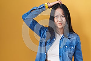Young asian woman standing over yellow background confuse and wondering about question
