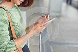 Young asian woman standing with suitcase and looking at mobile phone while waiting at the airport