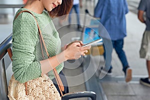 Young asian woman standing with suitcase and looking at mobile phone while waiting at the airport