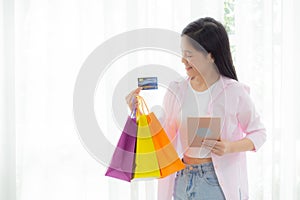 Young asian woman standing using digital tablet shopping online with credit card while holding paper bag.