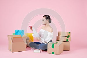 Young asian woman startup small business freelance sitting with parcel box, mobile and sale receipt on floor in living room at