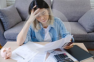 Young Asian woman is stressed because she looks at many expense bills and she has no money to pay credit card debt. She had a hand