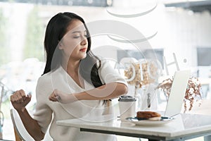 Young Asian woman stretches in a coffee shop while working on a laptop.