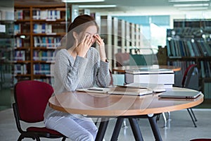 Young Asian woman student rubbing eyes, feeling tired after reading a book in library