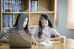 Young Asian woman student study and take notes with book in library. F