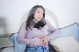 Young Asian woman suffering menses abdominal cramp - sick and tired Chinese girl lying on bed having having period pain holding photo