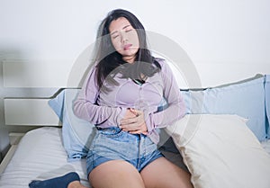 Young Asian woman suffering menses abdominal cramp - sick and tired Korean girl lying on bed having having period pain holding her