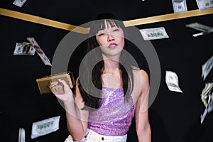 Young asian woman surrounded by dollar bills holding a toy gun.