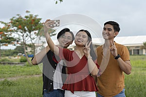 A young asian woman takes a selfie with two of her male friends. Having a fun casual pictorial at the park