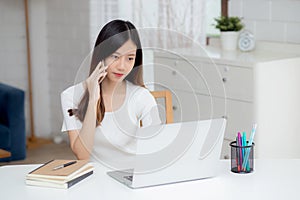 Young asian woman talking phone and work from home with laptop computer.