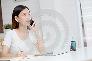 Young asian woman talking phone and work from home with laptop computer.