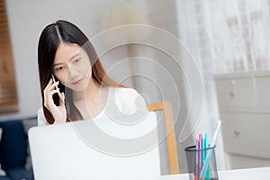 Young asian woman talking phone and work from home with laptop computer.
