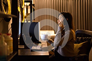 Young Asian woman talking on the phone while working from home late at night