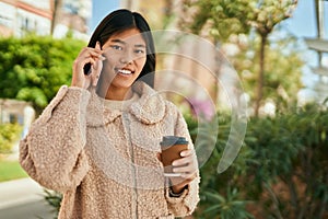 Young asian woman talking on the smartphone and drinking coffee at the city