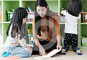 Young asian woman teacher teaching girls in kindergarten classroom, preschool education concept