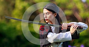 Young asian woman in traditional kimono trains in a fighting stance close-up portrait with katana sword samurai warrior girl in