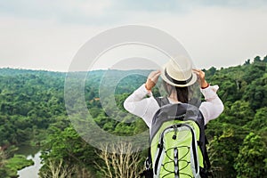 young asian woman traveler with backpack relaxing on mountian and looking forest