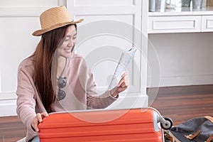 Young asian woman traveler prepare cloth and stuff into orange suitcase for holiday vacation at home.backpacker travel concept