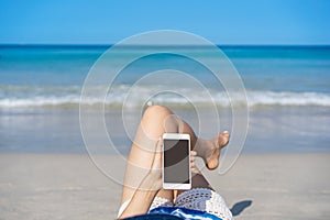 Young asian woman traveler using her smartphone and sunbath at tropical sand beach, Summer vacation