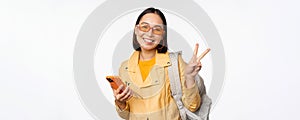 Young asian woman traveller, girl tourist in sunglasses, holding backpack and mobile phone, using application on