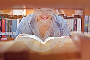 Young Asian woman university student reading book by bookshelf in college library for education