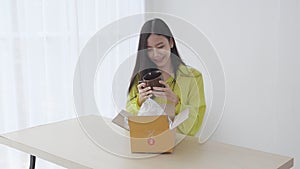 Young asian woman unpacking of parcel box with online shopping while satisfied at home, female opening package with purchase for