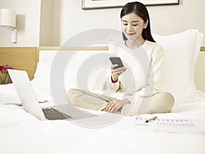 Young asian woman using cellphone and laptop on bed